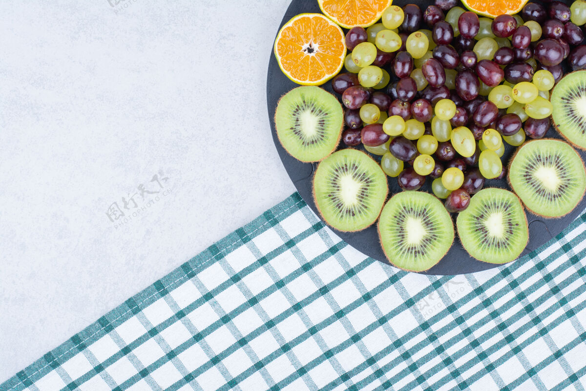 食物桌布上放满了葡萄 猕猴桃和橘子的深色盘子橙色猕猴桃水果