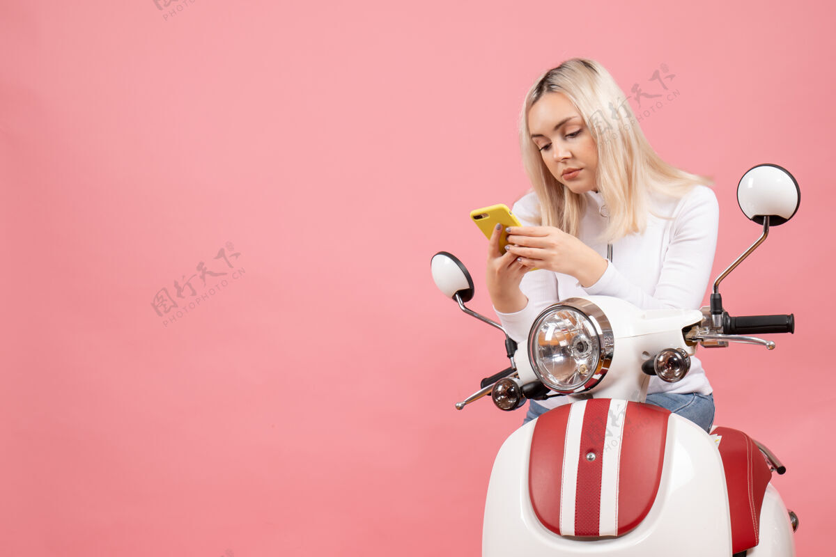 前排前视图：坐在轻便摩托车上看电话的年轻女士轻便摩托车时尚手持