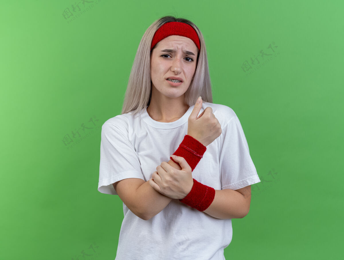 背带带着背带 戴着头带和腕带的疼痛的年轻运动女性 手被隔离在绿色的墙上人头带抱