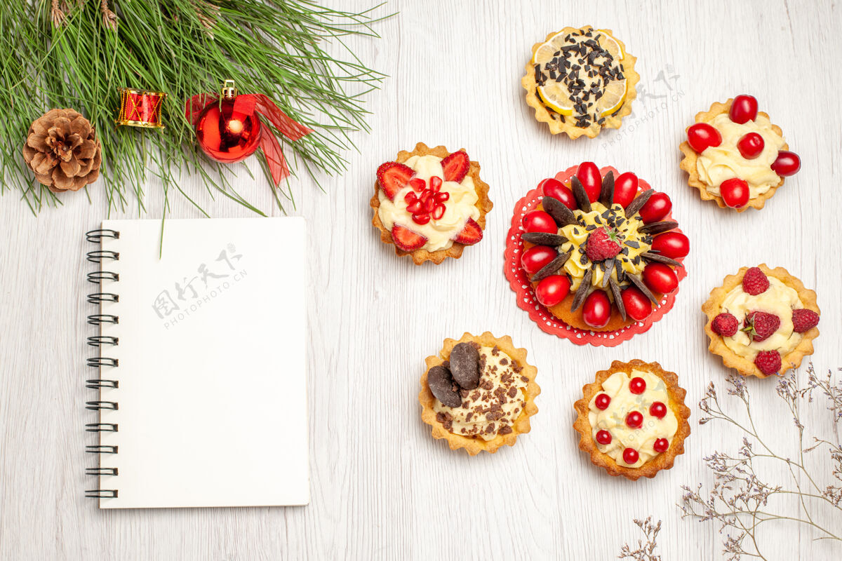 黄色顶视图浆果蛋糕圆形馅饼松树树叶圣诞玩具和一个笔记本上的白色木质地面食物橘子圣诞