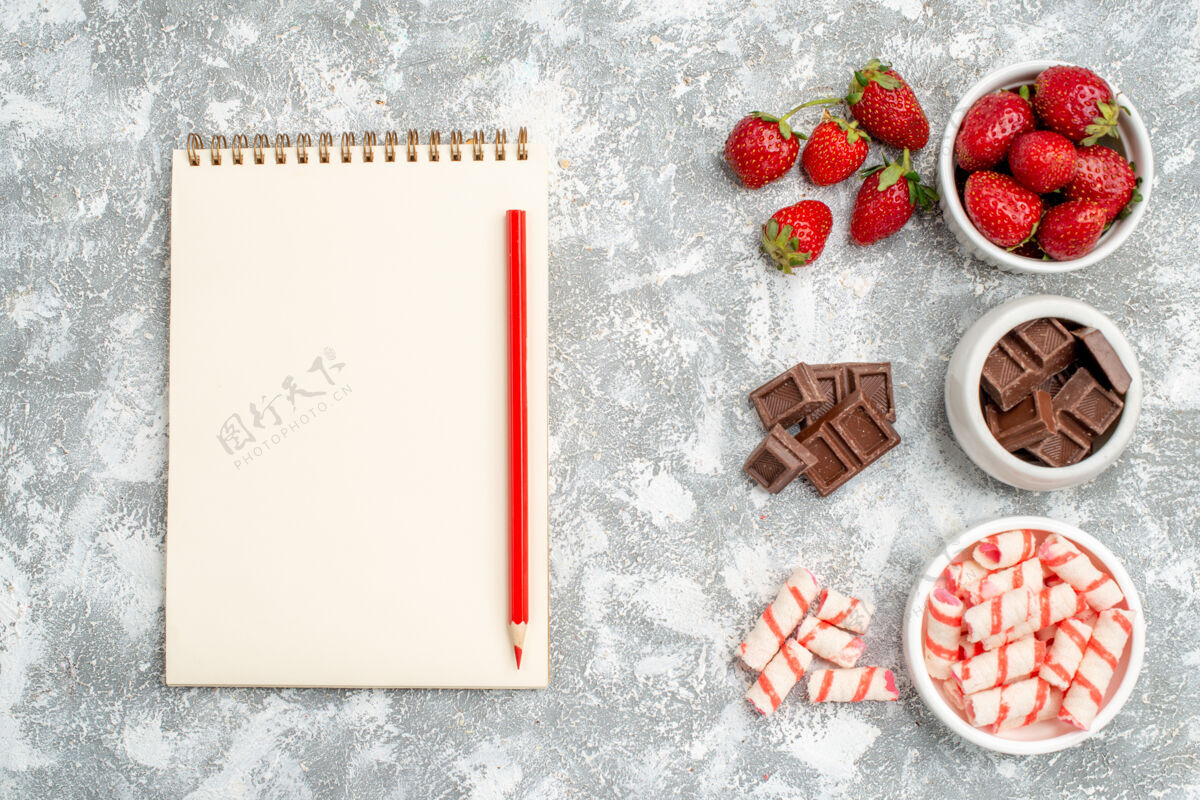 相框顶视图碗与草莓巧克力糖果和一些草莓巧克力糖果在右侧和笔记本与红铅笔在灰白的地面左侧左边笔记本草莓