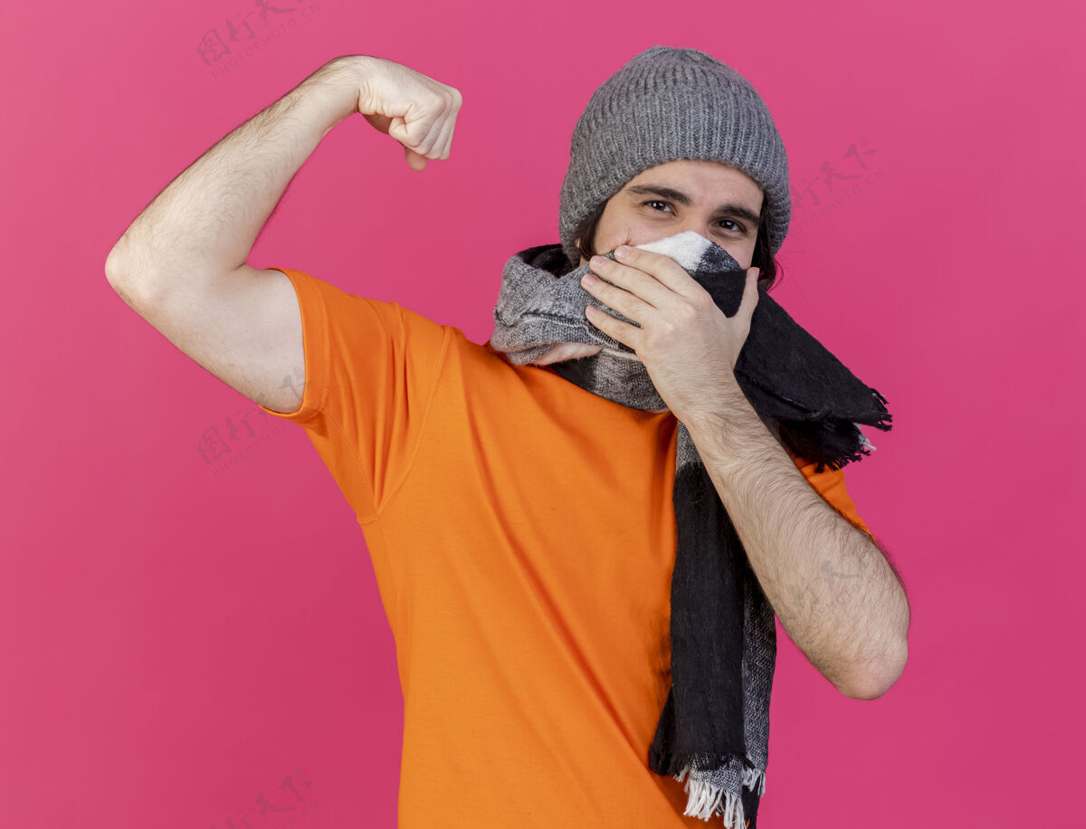 强壮年轻的病夫戴着冬天的帽子 戴着围巾 表现出强烈的姿态 脸上戴着隔离的粉色围巾帽子男人戴