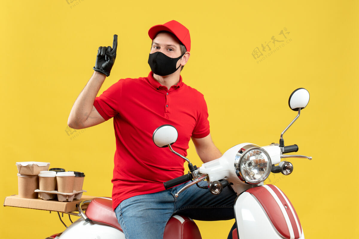 车辆顶视图自信的年轻人穿着红色上衣 戴着帽子 戴着手套 戴着医用面罩 坐在黄色背景上的踏板车上传递命令坐着命令交付