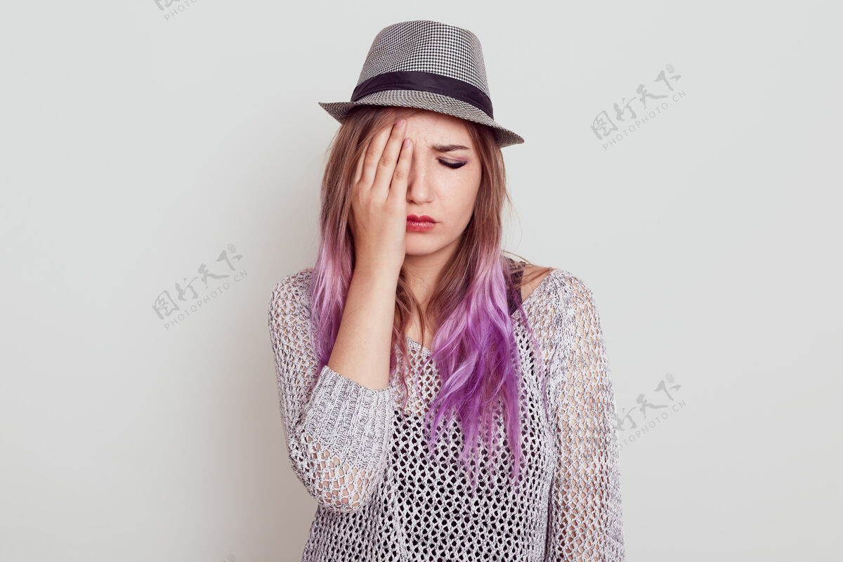 痛苦心烦意乱的美丽女人 淡紫色头发 穿着衬衫 戴着帽子 悲伤 用手掌遮住半张脸 闭着眼睛 隔着白墙困难坏情绪压力