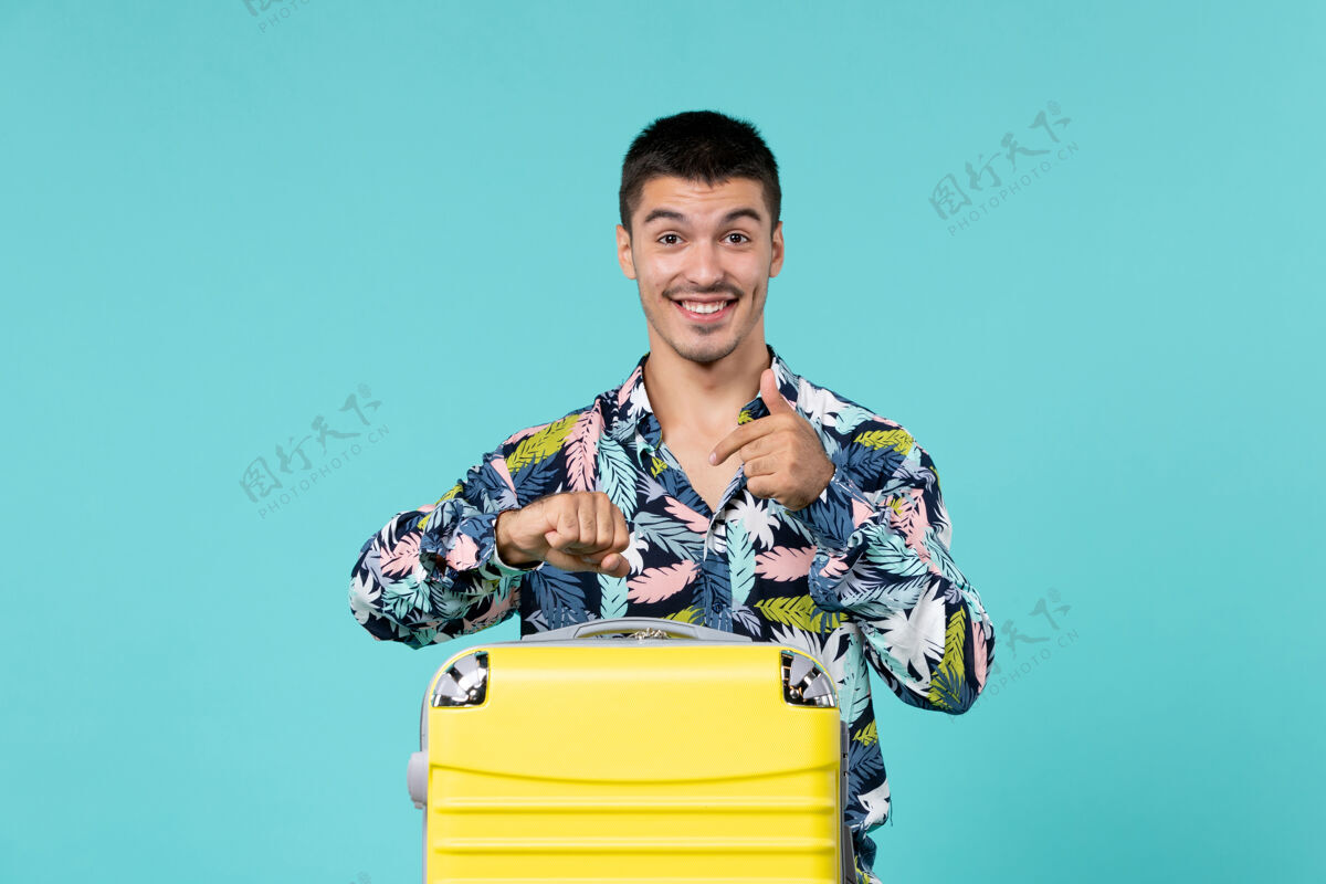 包年轻男子正准备度假 蓝色墙上挂着他的黄色包准备男人年轻的男人
