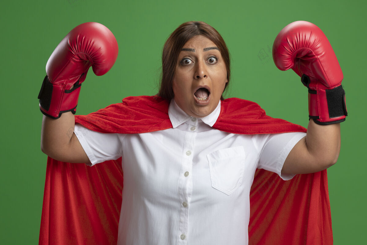 拳击吓得中年女超人戴着拳击手套举起双手孤立在绿色穿超级英雄女