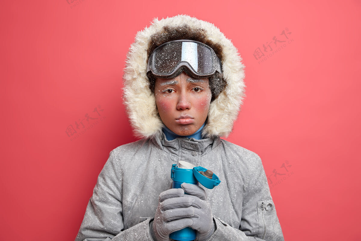 颤抖愁眉苦脸的冻僵女人捂着嘴唇 看起来心烦意乱 冬天运动后感到疲倦 喝着热饮料取暖 穿着外套和手套的她正在滑雪旅行兜帽室内非洲