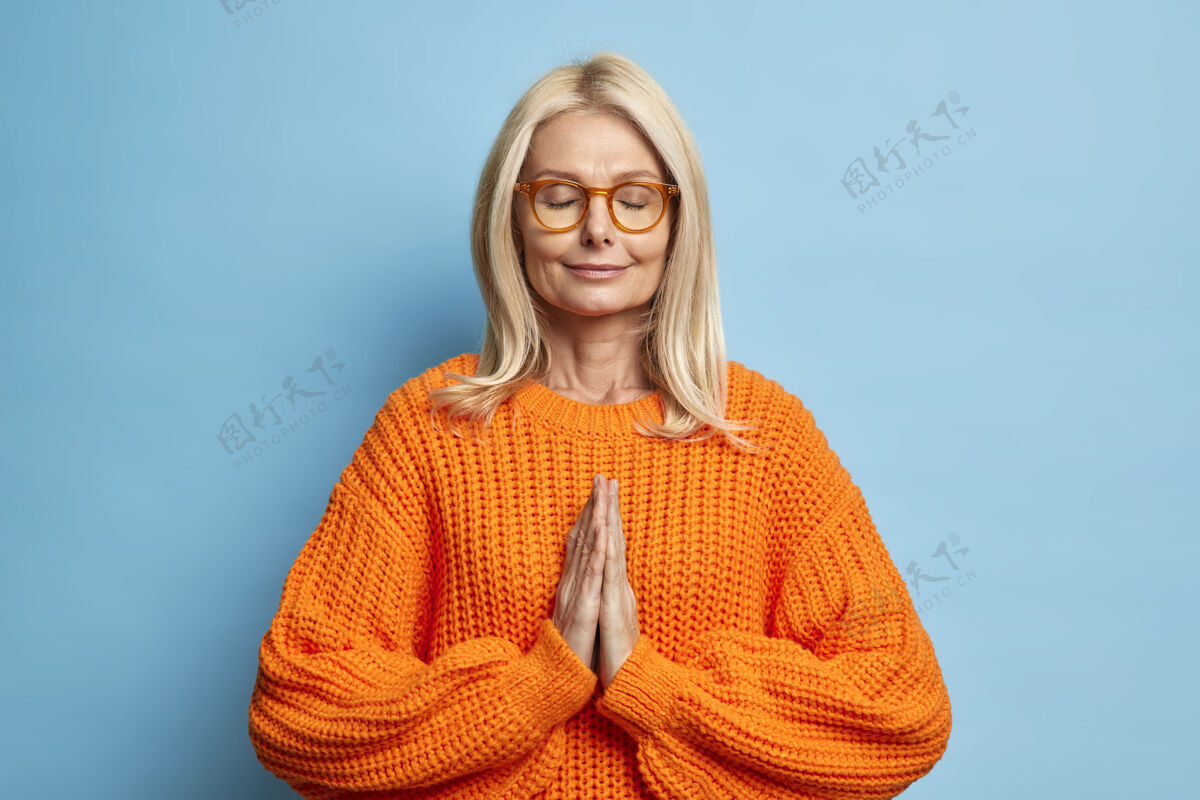 祈祷安静的金发女人闭着眼睛站在祈祷姿势祈祷身体健康穿着针织套头衫戴着眼镜老年人老年人人
