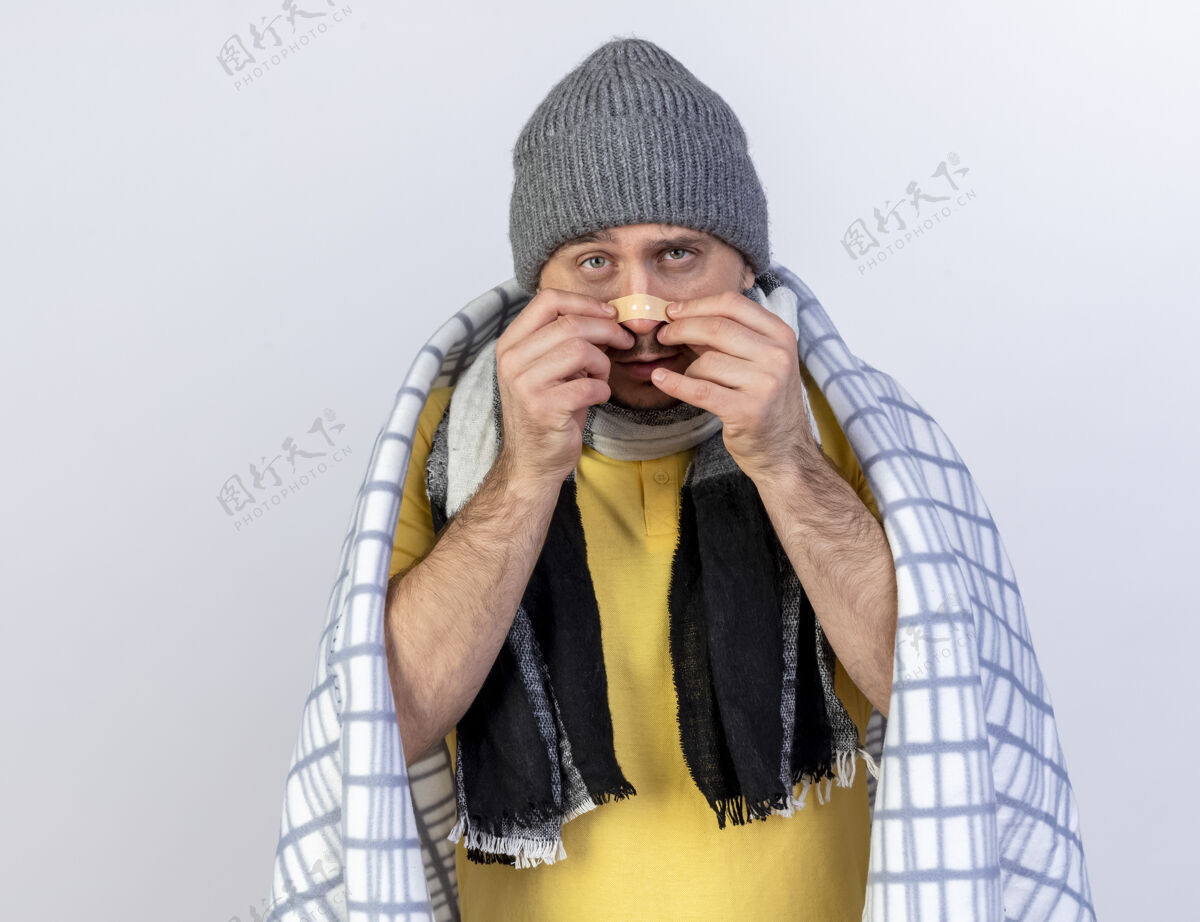 裹年轻的金发病斯拉夫男子戴着冬季帽子和围巾包裹在格子布放在鼻子上隔离医疗石膏白色墙壁与复制空间格子年轻人石膏