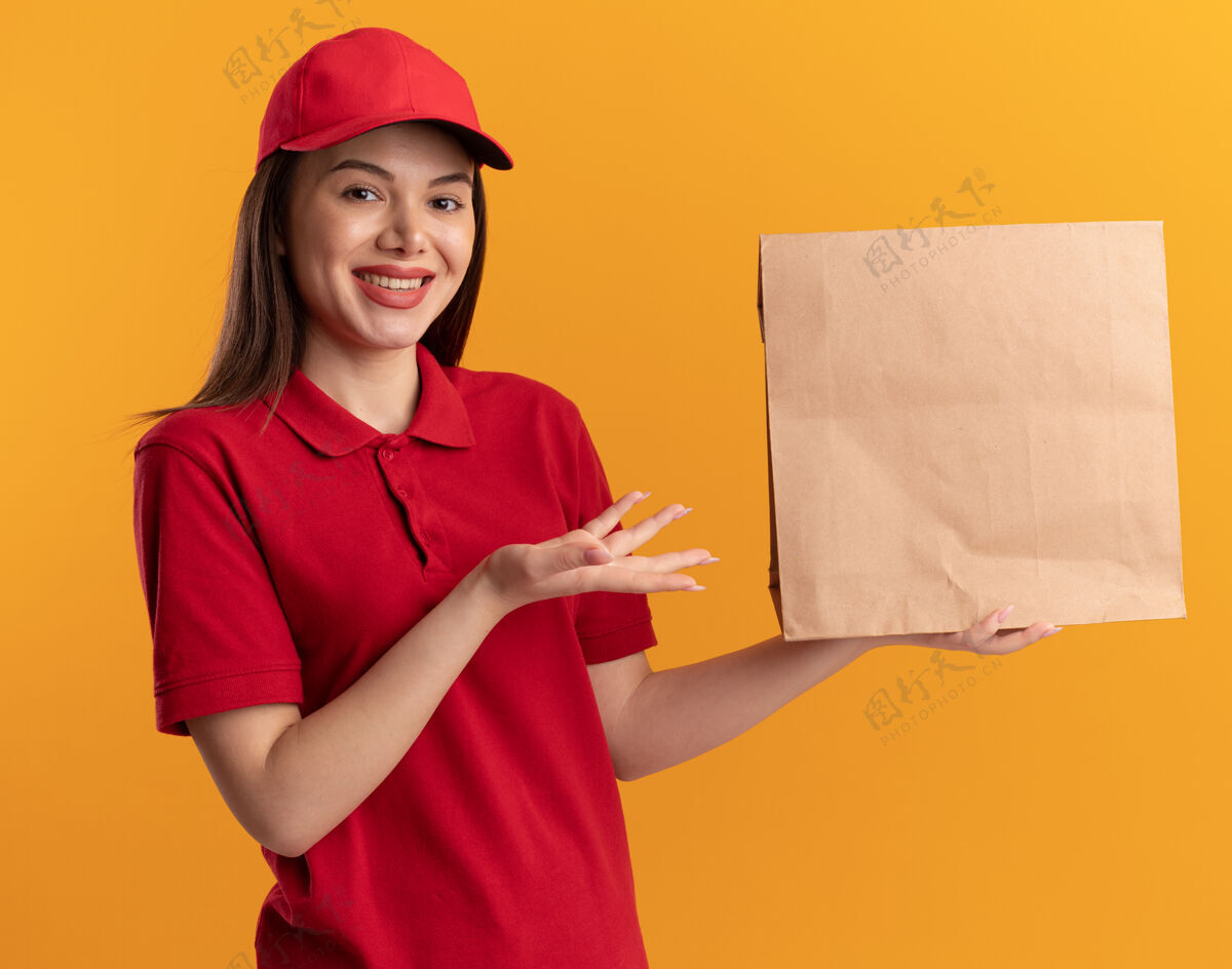 送货一个穿着制服 面带微笑的漂亮女送货员拿着并指着橙色的纸包装纸点制服