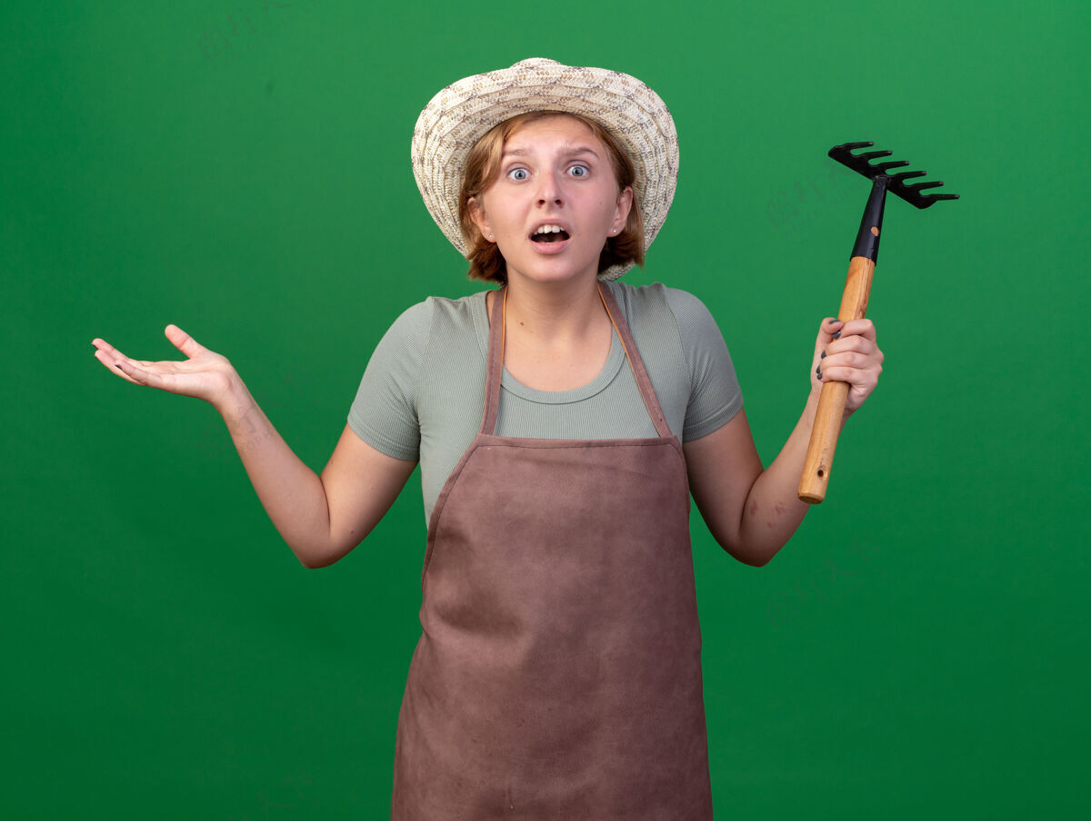 斯拉夫焦虑的年轻斯拉夫女园丁戴着园艺帽拿着耙子在草地上焦虑花园园艺