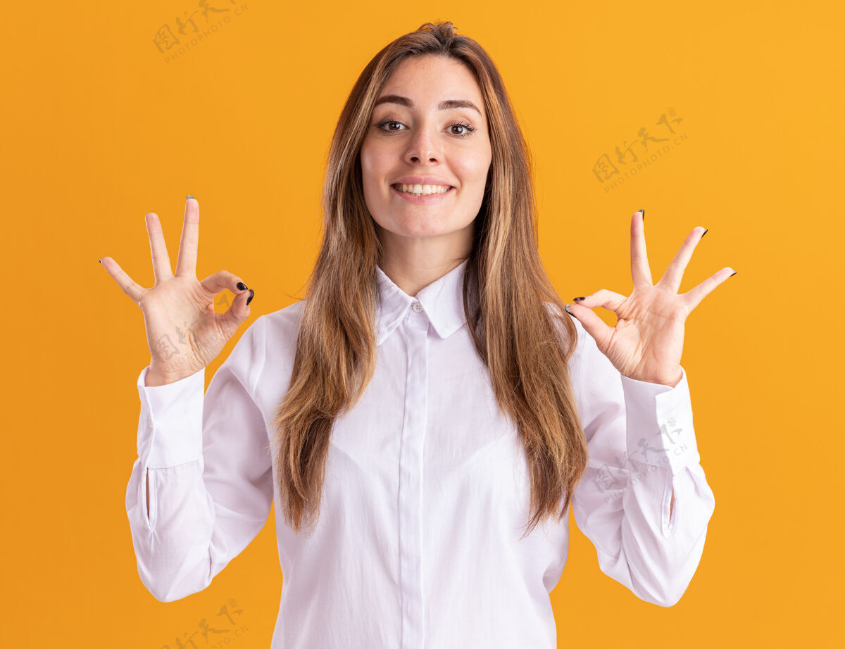 手年轻漂亮的高加索女孩微笑着用两只手在橙色上做手势表示同意好的年轻手势
