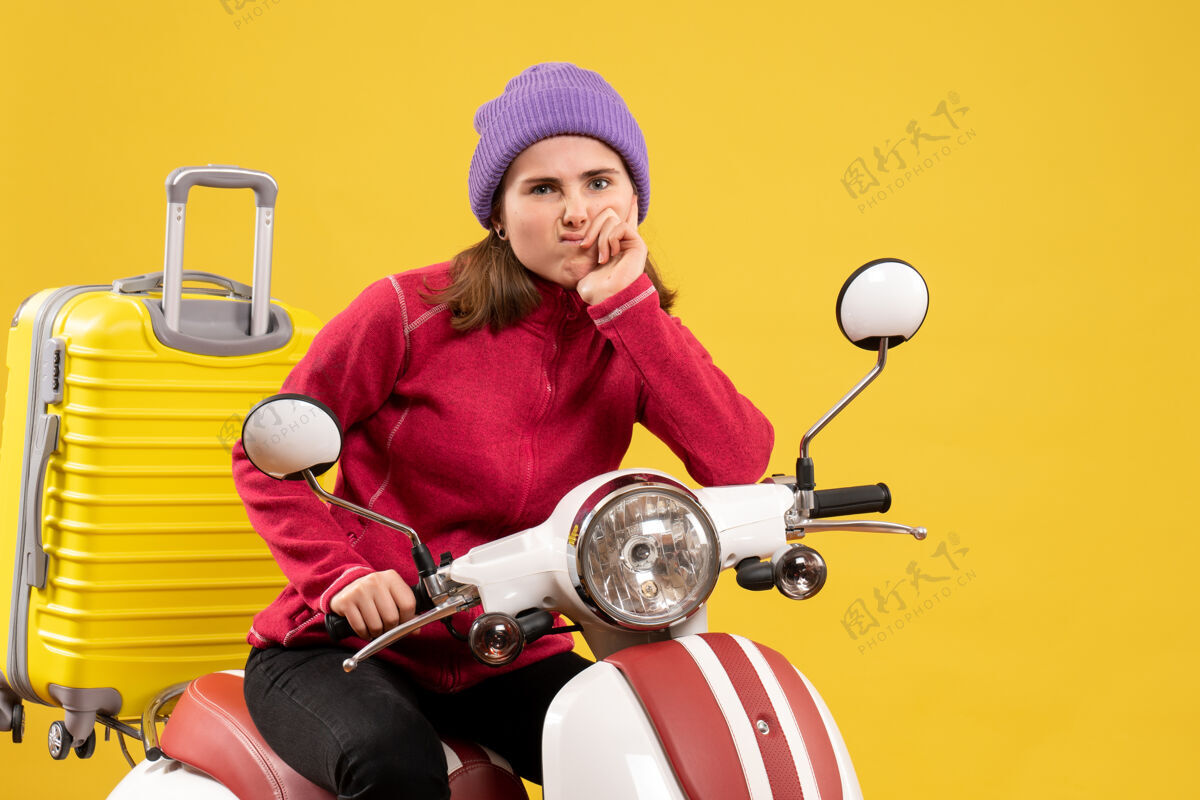 传送带前视图困惑的年轻女孩骑着轻便摩托车 提着黄色的手提箱快乐坐着轻便摩托车