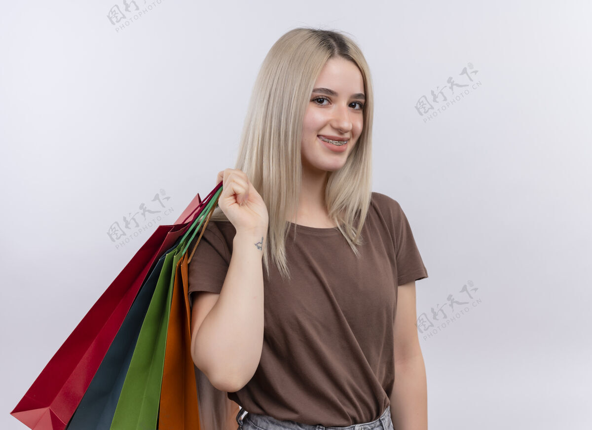 年轻微笑的金发女孩戴着牙套 肩上扛着购物袋 在一片空白的空间里复制微笑购物包
