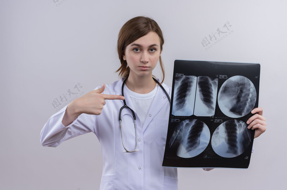 年轻面容严肃的年轻女医生穿着医用长袍 手持听诊器 拿着x光片指着它听诊器射击医生