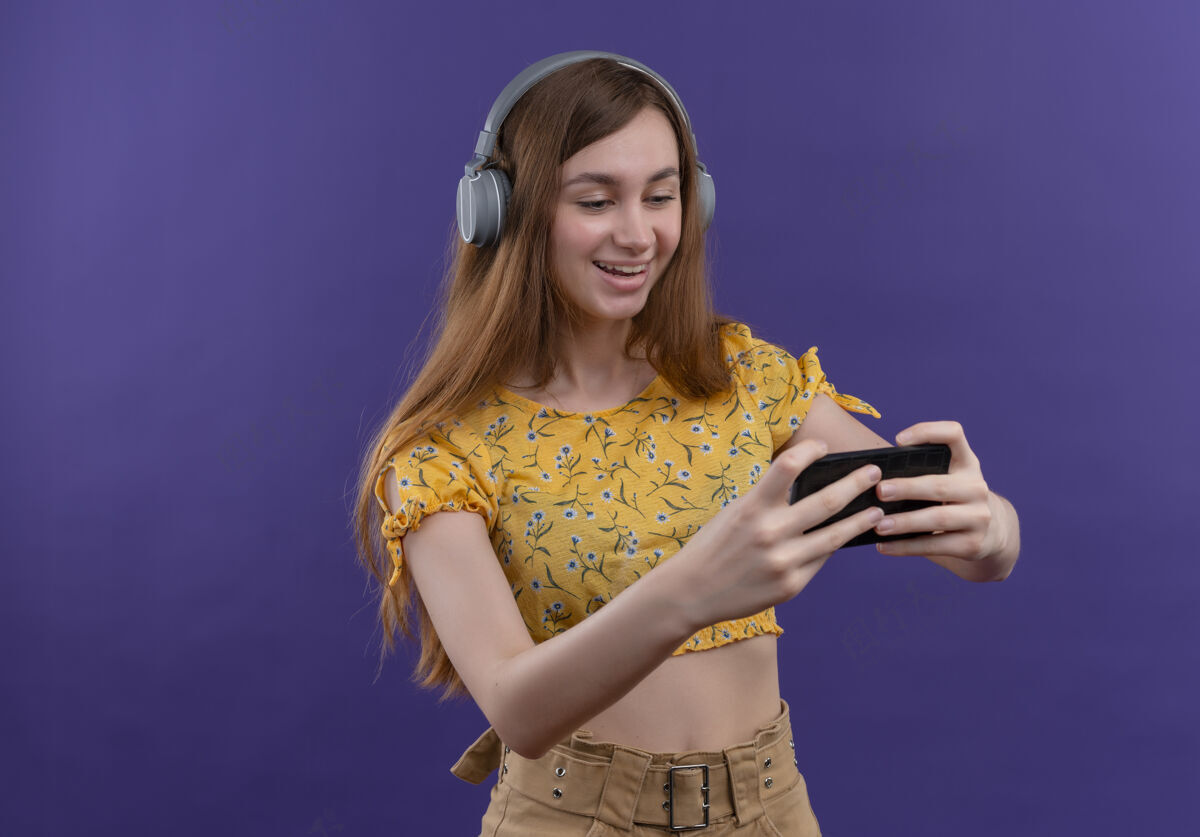 持有快乐的年轻女孩戴着耳机拿着手机在紫色的空间里与人隔绝复制年轻喜悦