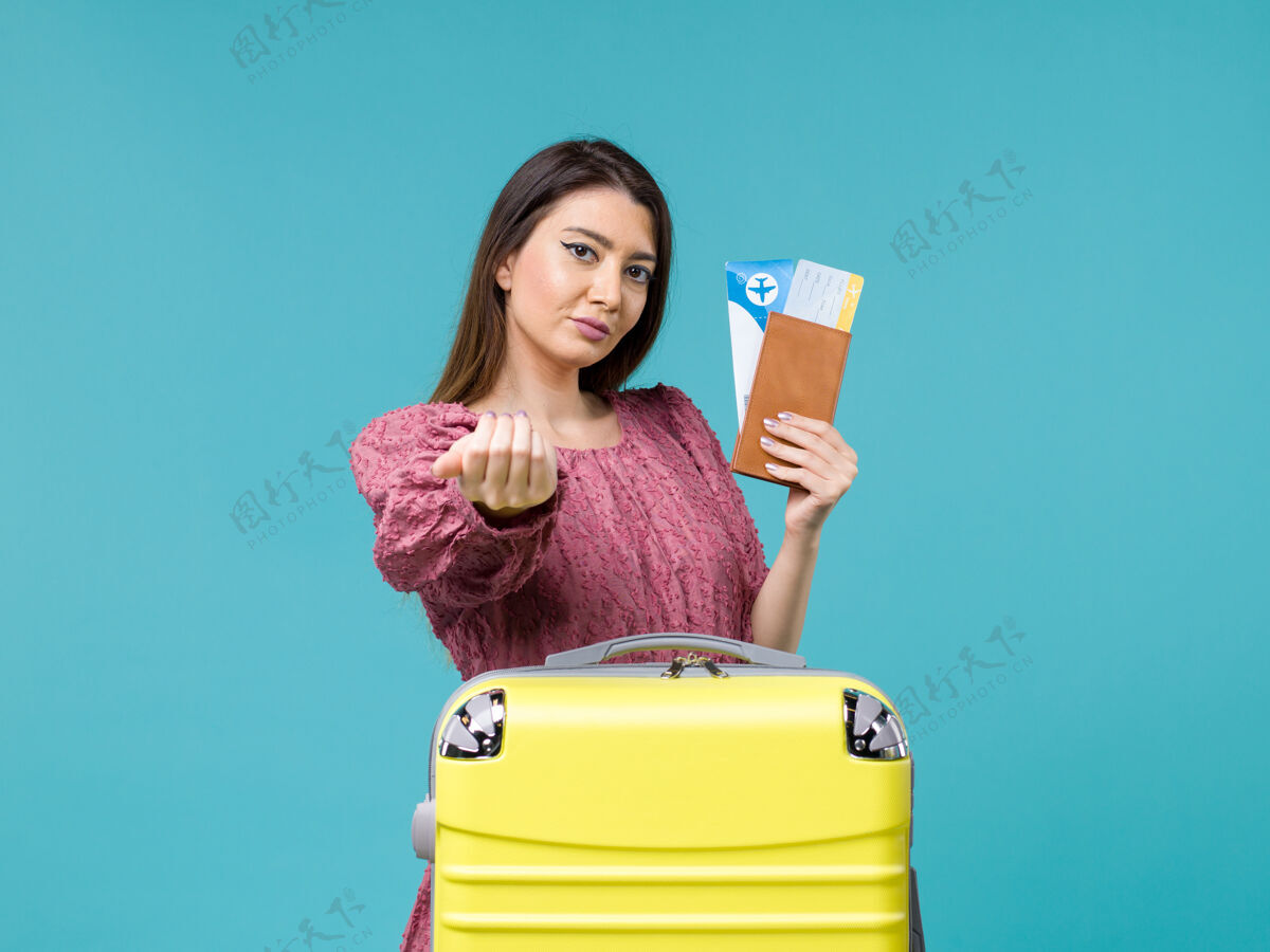 微笑前景度假中的女性拿着她的钱包和机票在蓝色背景上给某人打电话旅行女性暑假视图假期前面