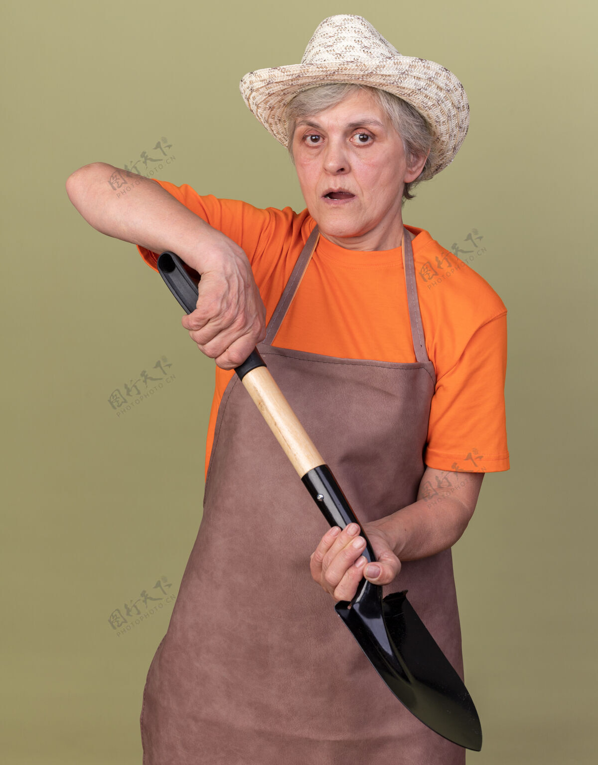 女焦虑的上了年纪的女园丁戴着园艺帽拿着铁锹在橄榄绿上黑桃园艺老人