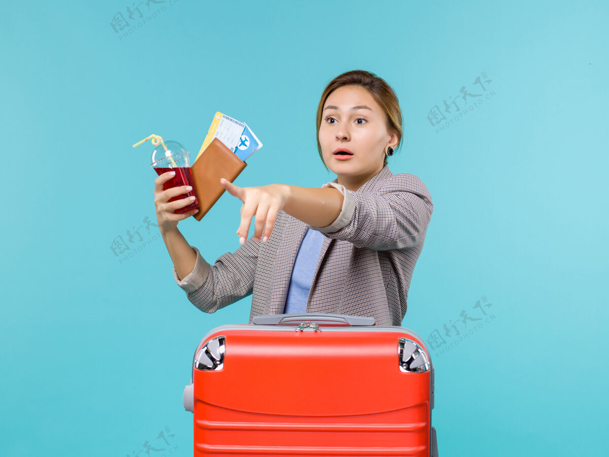 举行前视图：度假中的女性手持果汁和浅蓝色背景的机票旅行度假海上飞机微笑票旅行