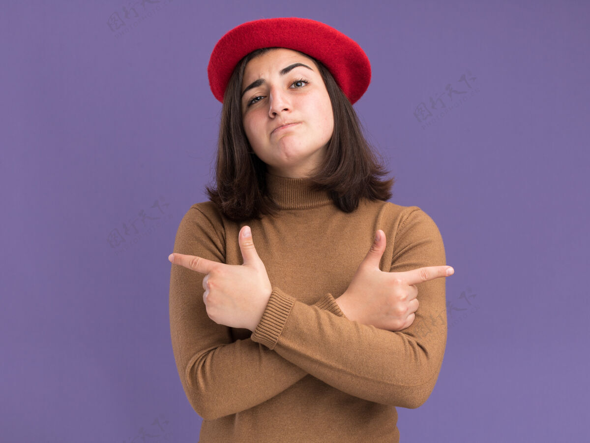 漂亮自信的年轻漂亮的白人女孩戴着贝雷帽指着紫色的两边贝雷帽紫色壁板