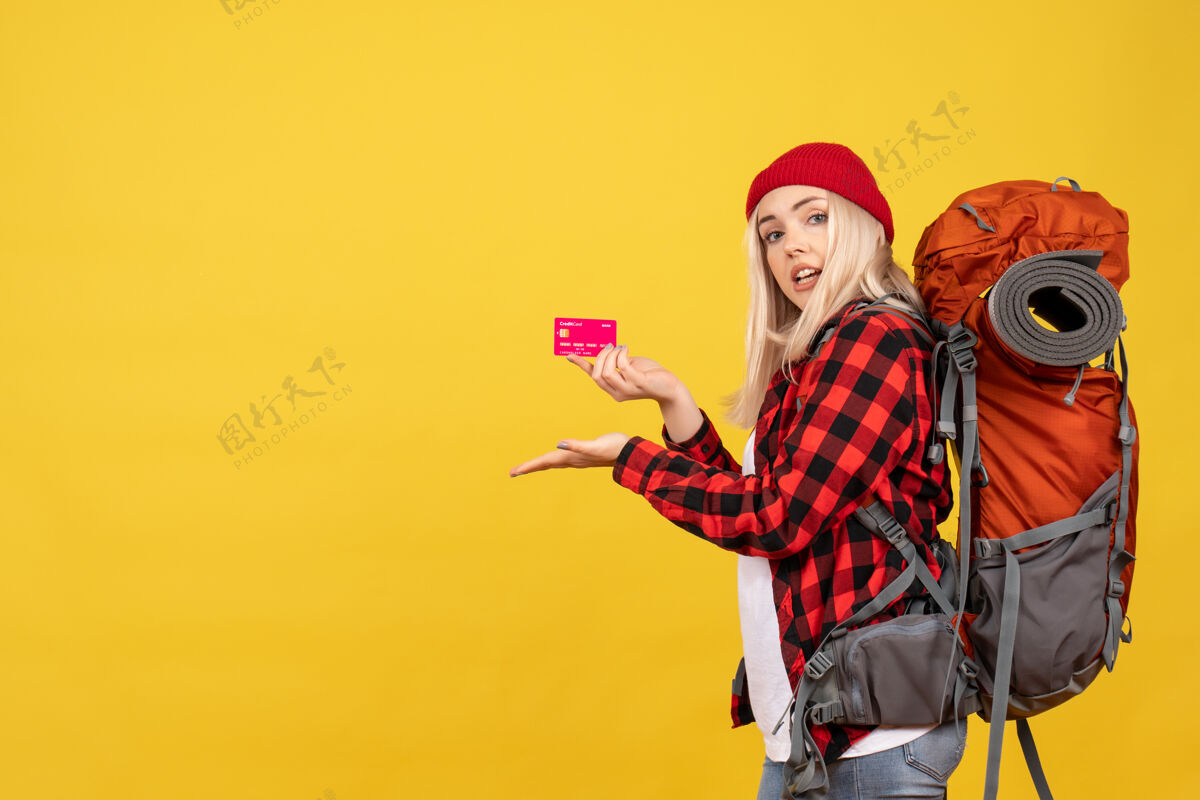 时尚正面图金发女孩背着背包拿着卡片在黄色的墙上人金发女孩快乐