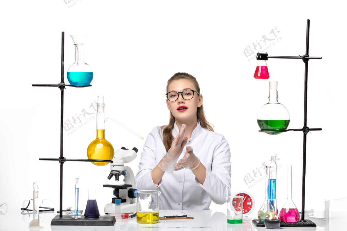 研究前视图穿着白色医疗服的女医生坐着工作 解决白色办公桌病毒冠状病毒大流行实验室白色女医生