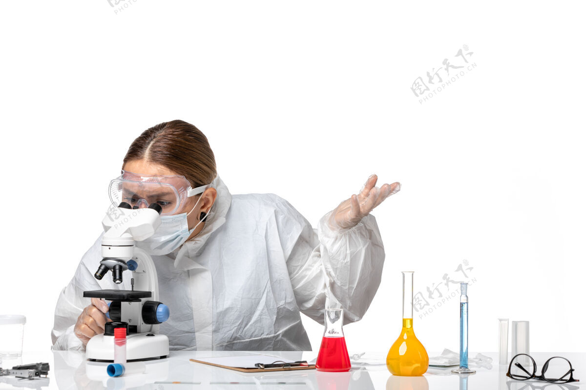 套装正面图女医生穿着防护服 戴着口罩 用显微镜观察淡白色背景上的健康大流行病毒冠状病毒正面灯光病毒