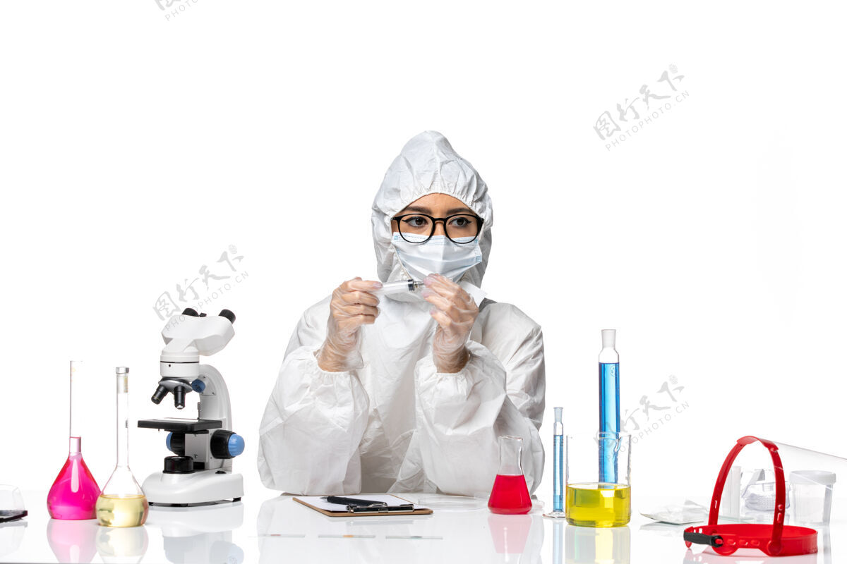 西装正面图身着特殊防护服的女化学家拿着针剂在浅白的办公桌上化学冠状病毒大流行病毒桌子男人