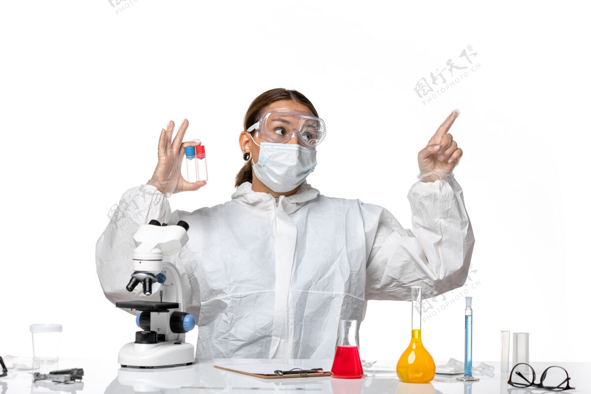 视图正面图：穿着防护服 戴着口罩的女医生拿着浅白色背景的空烧瓶 身上有冠状病毒实验室外套防护健康