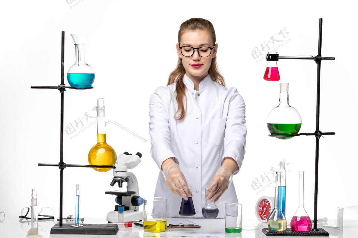 医学前视图穿着医疗服的女化学家在白色办公桌上用不同的解决方案化学大流行的冠状病毒视野人办公桌