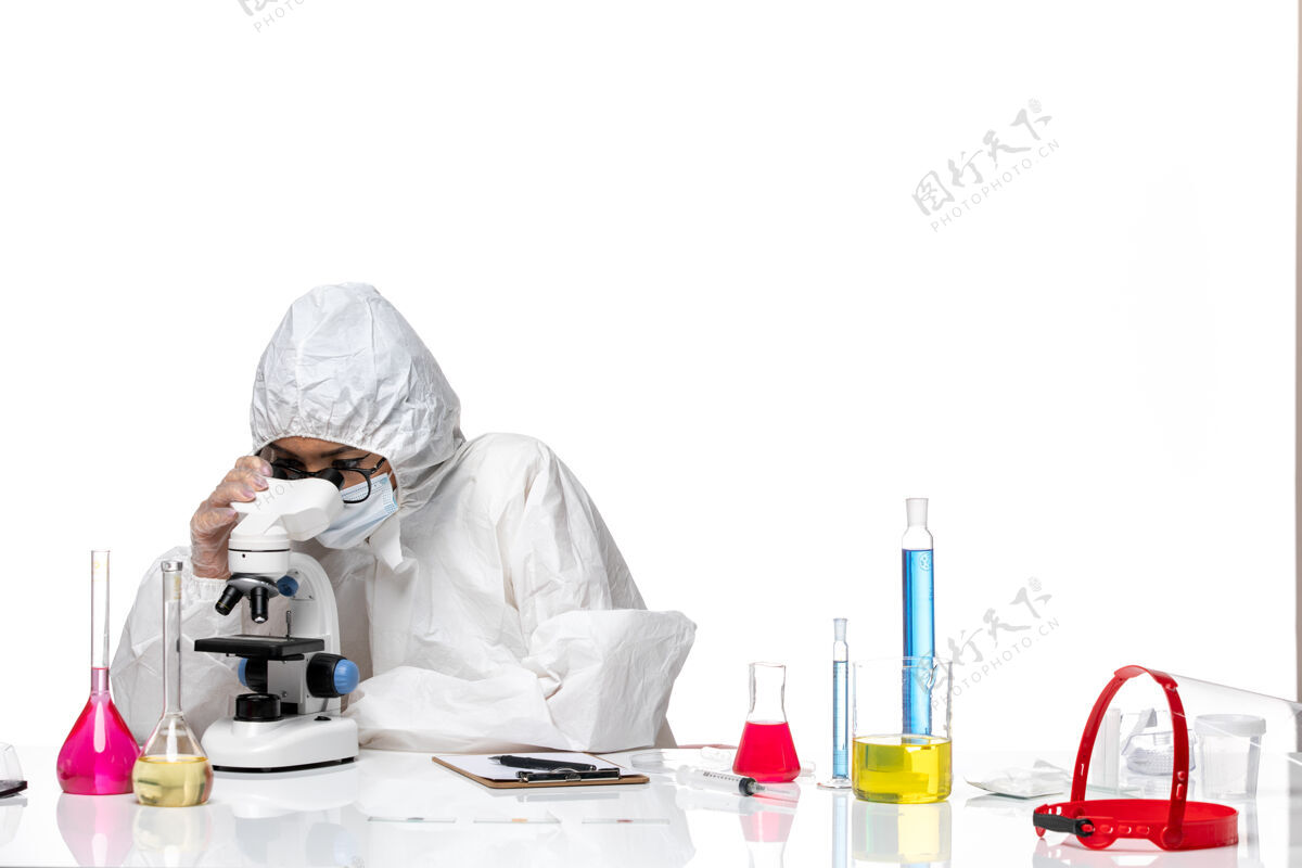 医疗前视图穿着特殊防护服的女化学家在白色背景上用显微镜检查样本化学冠状病毒-大流行性健康病毒样品防护医生