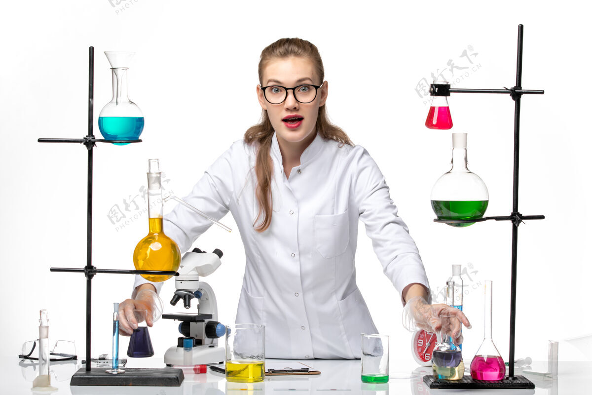 工作前视图穿着医疗服的女化学家在白色背景上用不同的溶液工作化学大流行性冠状病毒正面专业人