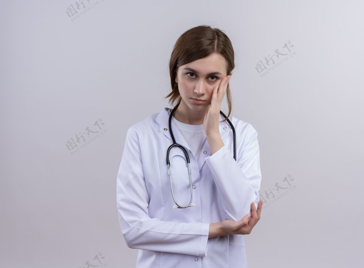 医学无聊的年轻女医生穿着医用长袍和听诊器 手放在脸颊和复印空间长袍无聊听诊器