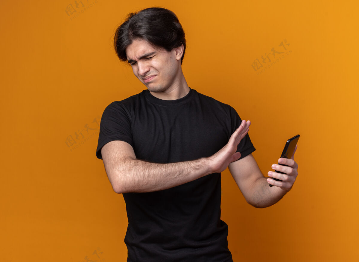 姿势闭着眼睛的神经质年轻帅哥穿着黑色t恤拿着一只手拿着手机隔着橙色的墙上站着电话感觉