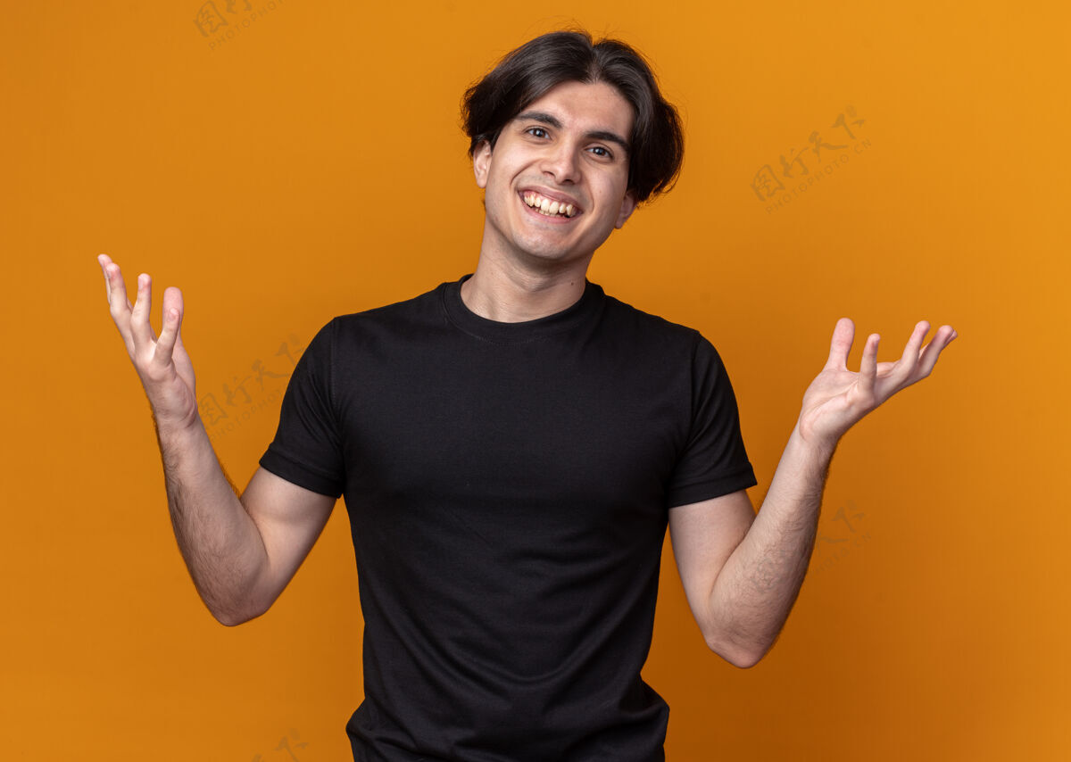手微笑着的年轻帅哥穿着黑色t恤摊开双手孤立在橙色的墙上年轻市民表情