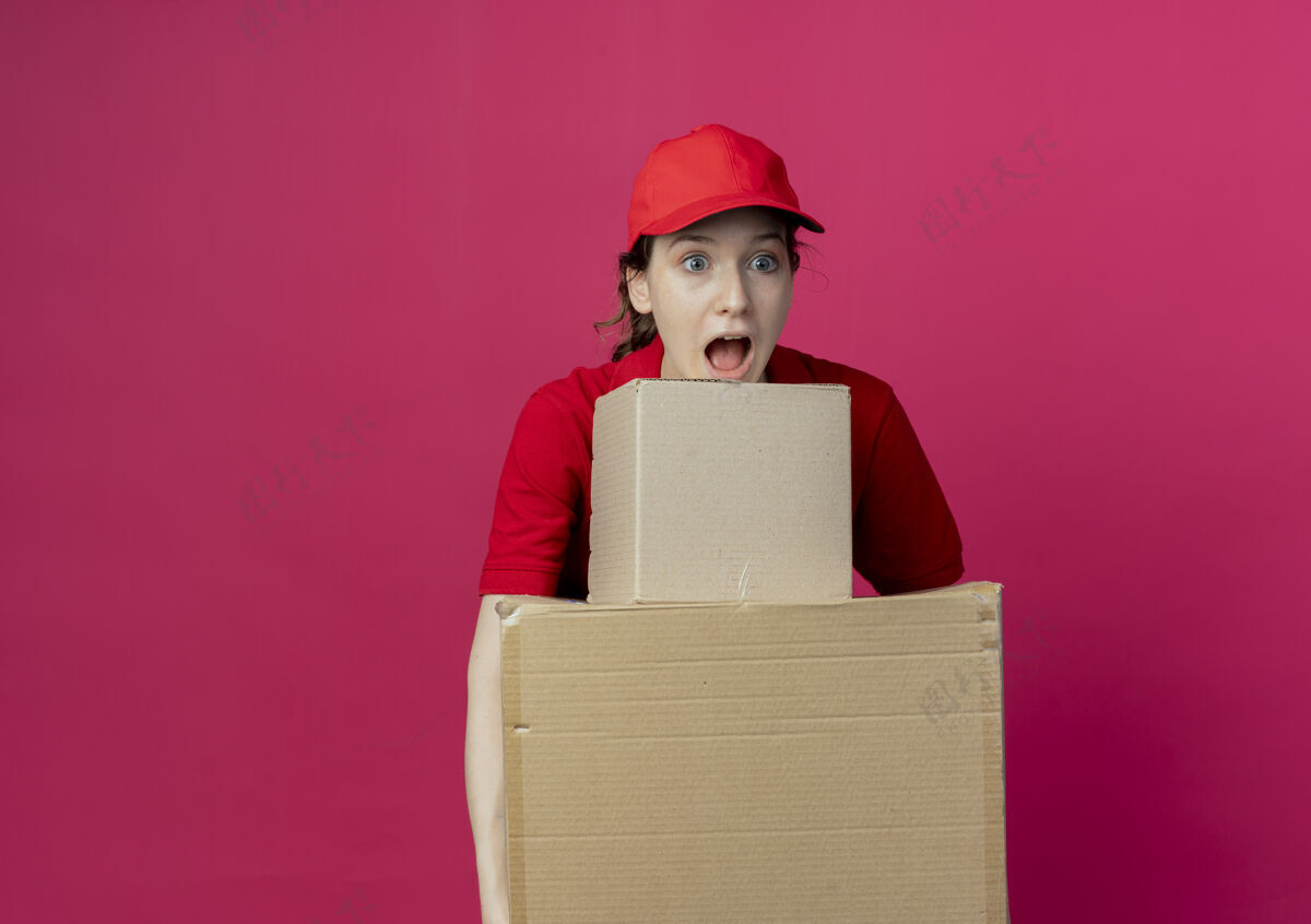 制服令人印象深刻的年轻漂亮的送货女孩在红色制服和帽子举行纸箱看直红色背景与复制空间孤立送货背景帽子