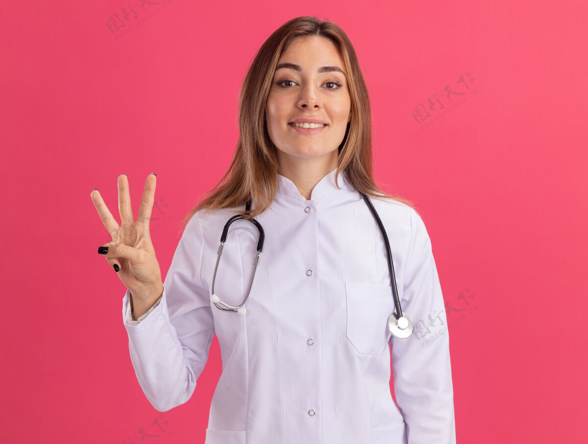 穿着微笑的年轻女医生穿着医用长袍 听诊器显示粉红色墙上有三个孤立的人微笑衣服长袍