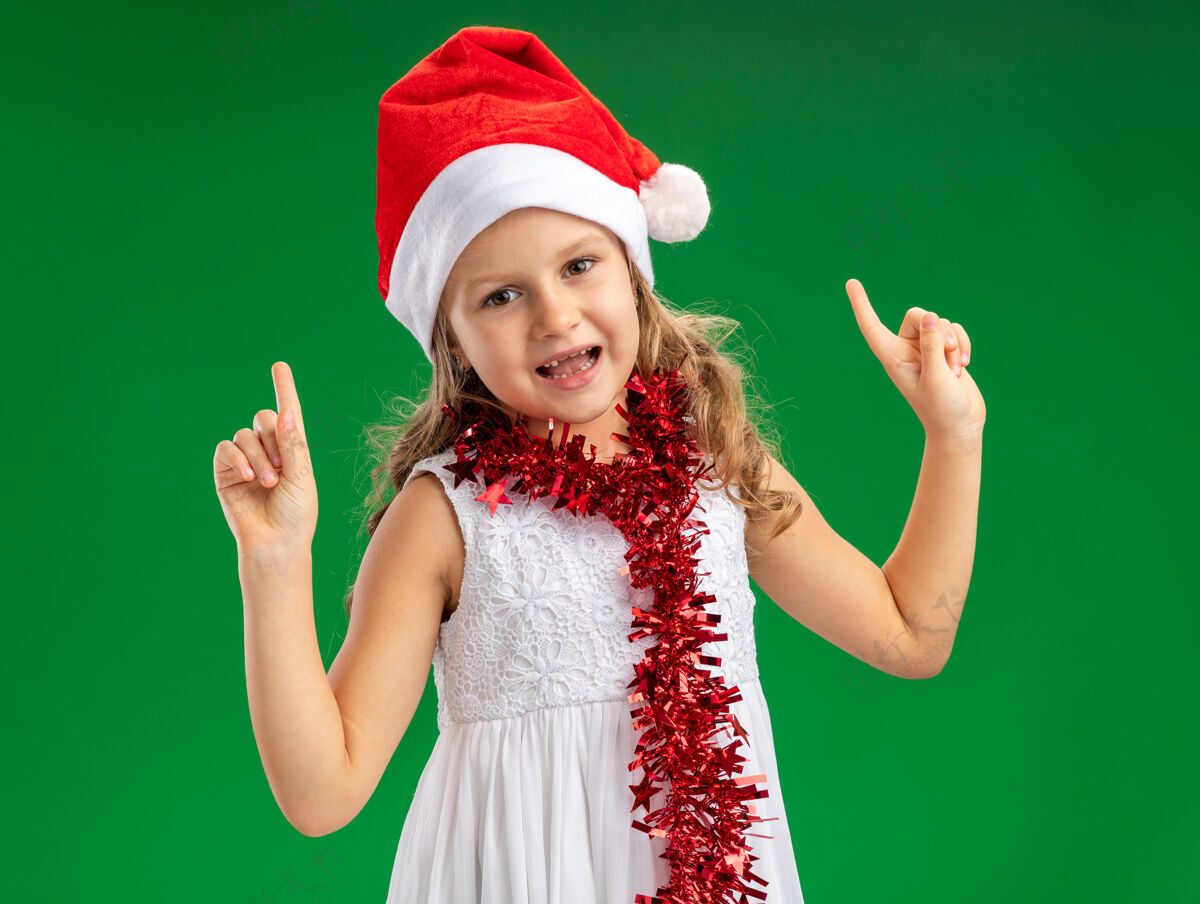 小给人印象深刻的小女孩戴着圣诞帽 脖子上点着花环 在绿色的背景上孤立起来向上女孩圣诞节