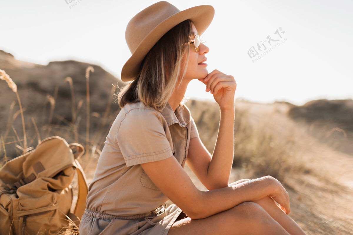 冒险穿着卡其色长裙 戴着帽子 背着背包 在沙漠的沙滩上旅行的美丽时尚的年轻女子时尚自然旅游