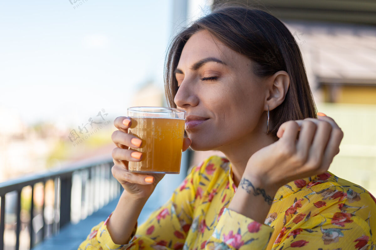 刷新穿着盛装的女人在夏日咖啡馆里享受着清凉的康普茶啤酒 闭着眼睛嗅着味道食物摇摆茶