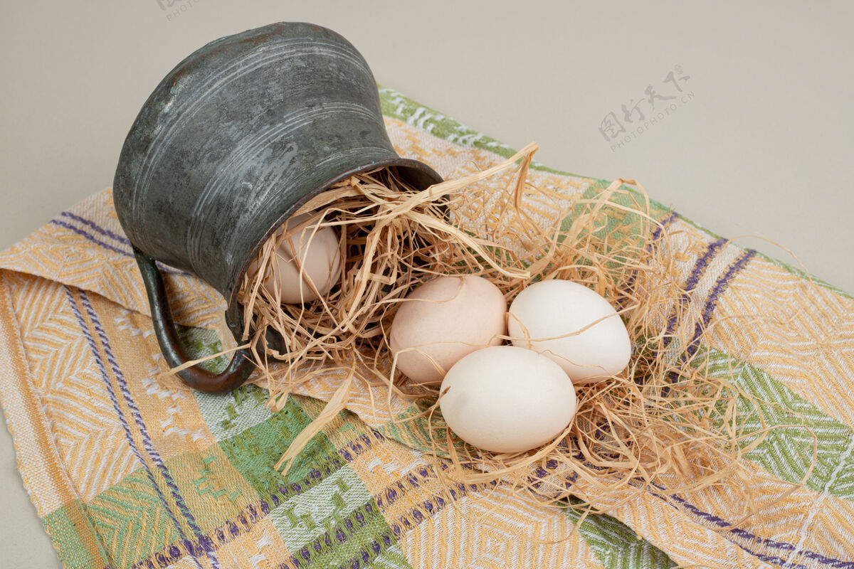 生的新鲜的鸡蛋和干草放在桌布上的古代杯子里鸡蛋鸡肉水壶