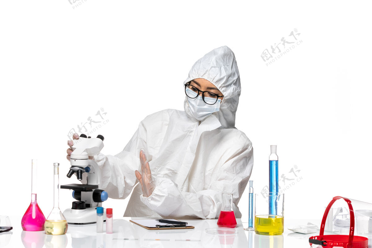 显微镜前视图穿着特殊防护服的女化学家在白色背景的化学病毒实验室里用显微镜工作诊所白人医生