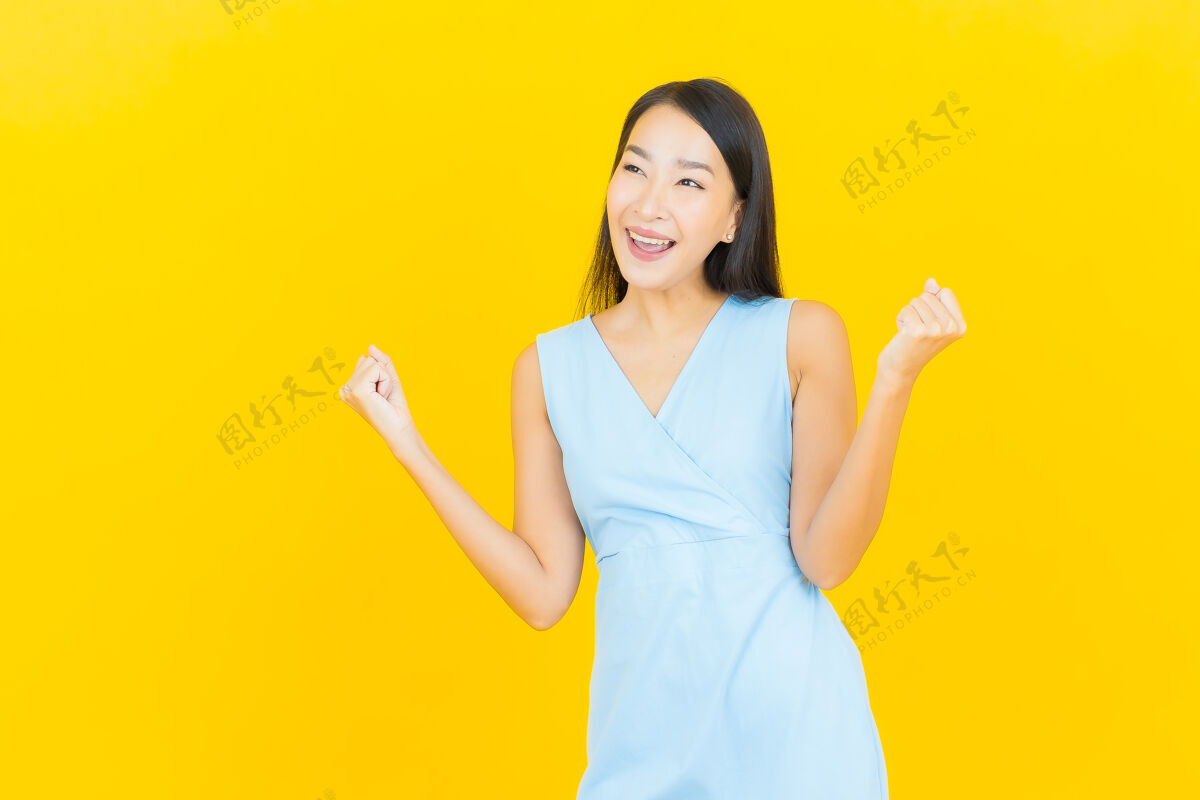 时尚在黄色墙壁上描绘美丽的亚洲年轻女子微笑的动作人穿着年轻