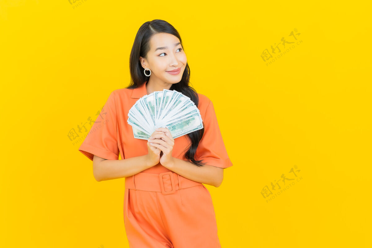 美元肖像美丽的亚洲年轻女子微笑着在黄色上有很多现金和金钱财务储蓄收入