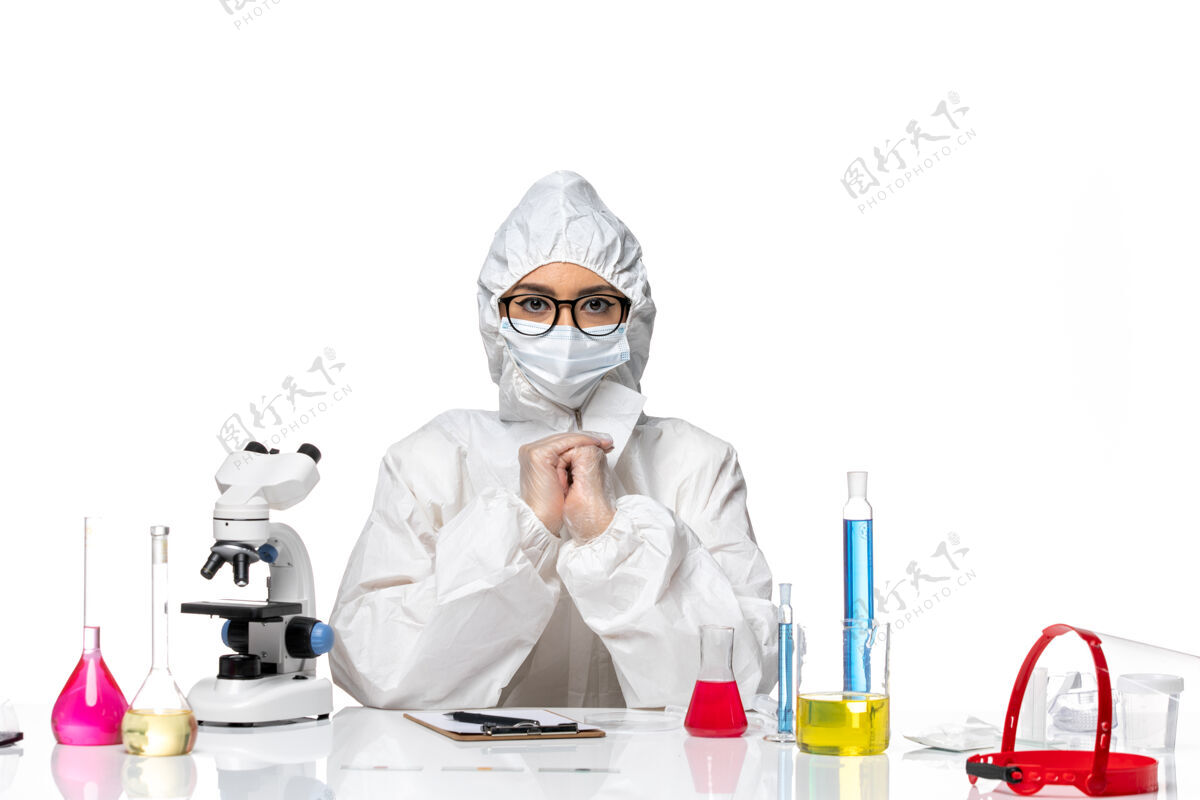 健康前视图穿着特殊防护服的女化学家坐在白色化学背景上的解决方案-病毒大流行专业坐姿口罩