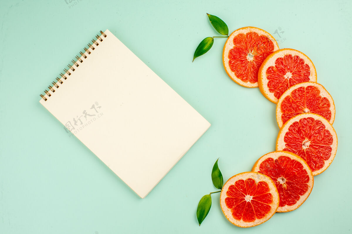 健康美味的新鲜葡萄柚 多汁的水果切片 浅蓝色表面上有记事本纸张食品节日