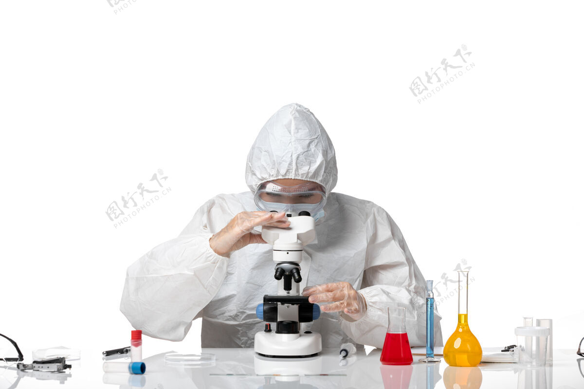 视图前视图：女医生穿着防护服 戴着口罩 在显微镜下观察因病毒感染而引起的浅白色背景病毒大流行的健康病毒专业科学家实验室