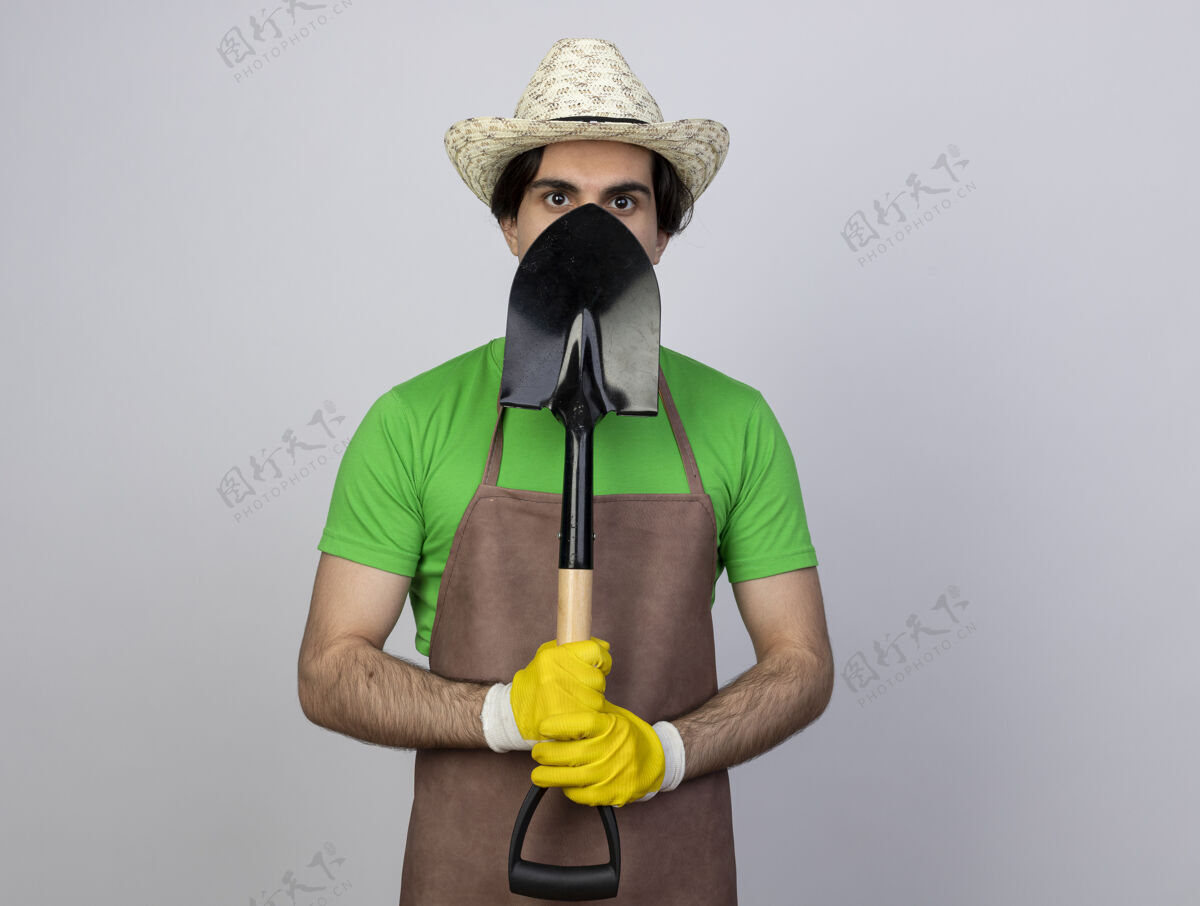 家伙穿着制服的年轻男园丁戴着园艺帽和手套 用铁锹遮住脸男人男人盖