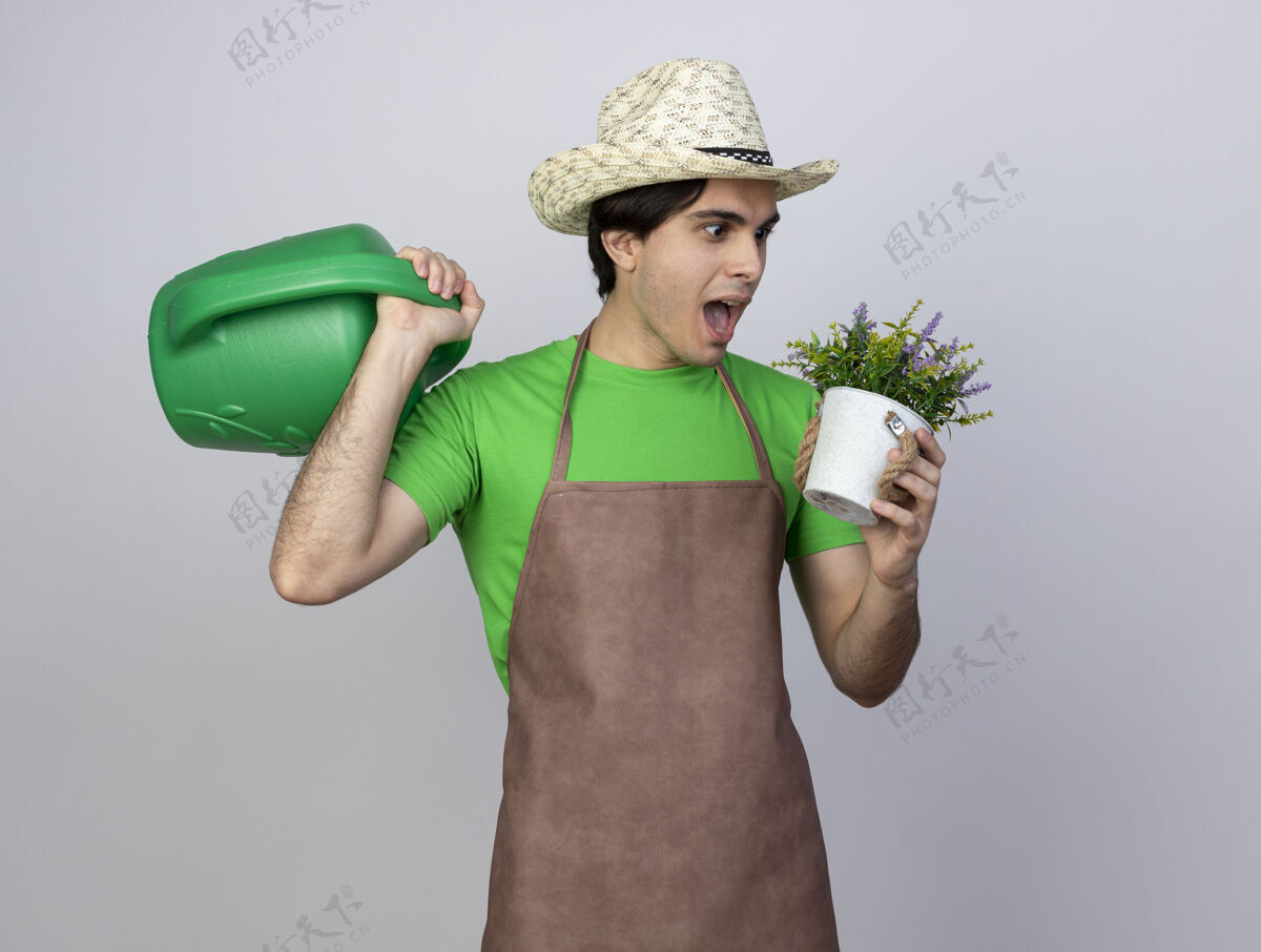 肩膀一个穿着制服的年轻男园丁惊讶地戴着园艺帽 肩上扛着水罐 手里拿着花盆里的花穿手人