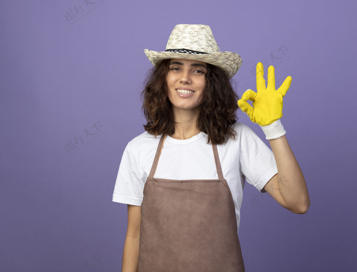 人年轻的女园丁微笑着穿着制服 戴着园艺帽和手套 表现出良好的姿态年轻制服手势